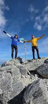 Two climbers with arms raised on the summit of Mytikas